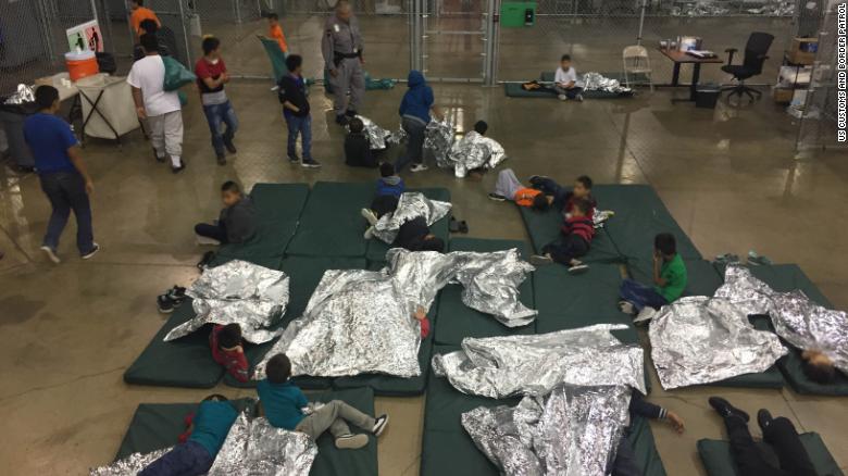 a bunch of children inside a chain-link fence enclosure, with space blankets